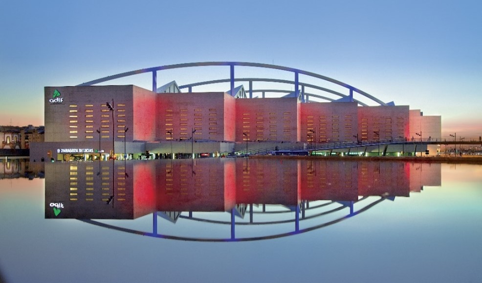 Estación Delicias de Zaragoza. edificio moderno, iluminado de rojo, reflejado sobre el agua de una fuente. 